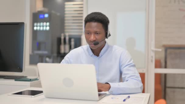 非洲男人带着耳机在呼叫中心的笔记本电脑上工作 — 图库视频影像