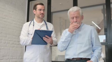 Öksüren yaşlı adam doktorla sağlık sorunlarını tartışıyor.