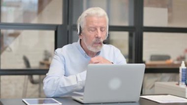 Kulaklıklı yaşlı adam, Çağrı Merkezi 'nde laptopta görüntülü sohbet yapıyor.
