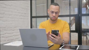 Laptop 'ta çalışan ve akıllı telefon kullanan İspanyol bir adam.