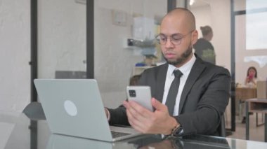 Karışık Yarış İşadamı Dizüstü bilgisayarda çalışıyor ve akıllı telefon kullanıyor.