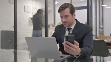 Orta yaşlı iş adamı Laptop 'ta çalışıyor ve akıllı telefon kullanıyor.