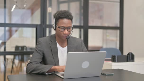 头戴耳机的非裔美国人在笔记本电脑上工作时看着相机 — 图库视频影像