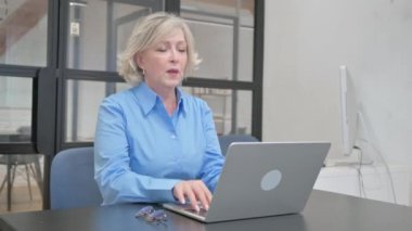 Ofiste dizüstü bilgisayar kullanan yaşlı bir kadın öksürüyor.