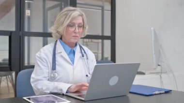 Senior Female Doctor Typing on Laptop