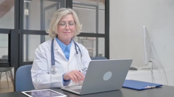 Médica Sênior Apontando Para Câmera Enquanto Trabalhava Laptop — Vídeo de Stock