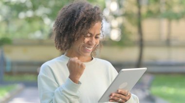 Young African Woman Celebrating Success on Tablet Outdoor