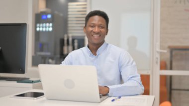 Ofiste Dizüstü bilgisayarla çalışırken kameraya gülümseyen Afrikalı İşadamı