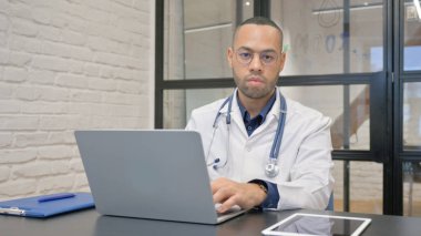 İspanyol doktor laptopta çalışırken kameraya bakıyor