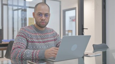 Laptop 'ta çalışırken kameraya bakan İspanyol genç adam.