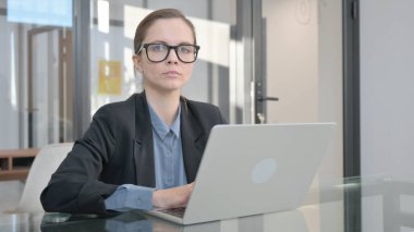 Genç İş Kadını Ofiste Dizüstü bilgisayarla çalışırken Kameraya Bakıyor