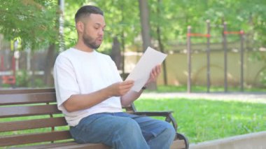 Açık havada oturan orta yaşlı adam belgeleri okurken kutlama yapıyor