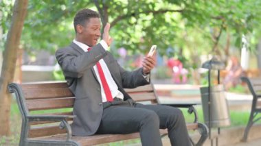 Açık havada otururken Afrikalı İş Adamı Akıllı Telefonla Video Sohbeti Yapıyor