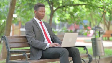 Afrikalı İşadamı kucağında laptopla kameraya bakıyor.