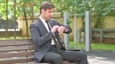 Genç İş Adamı Dışarıda Oturuyor ve Akıllı Seç Kullanıyor