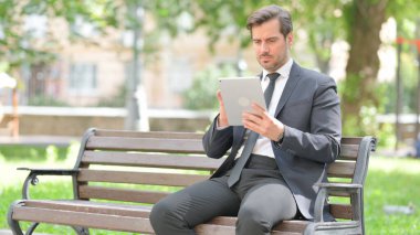 Orta yaşlı işadamı Bench 'te otururken dijital tablet kullanıyor.