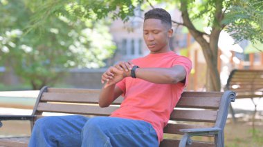 Bench 'in dışında beklerken gelişigüzel Afrikalı Adam Zamanı Kontrol Ediyor