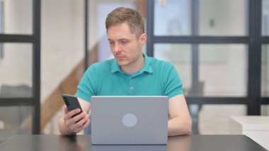 Olgun Yetişkin Adam Dizüstü bilgisayarda çalışıyor ve Akıllı Telefon Kullanıyor