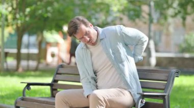 Park 'ta otururken sırt ağrısı çeken sıradan bir genç adam.