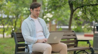 Dışarıdaki Laptop 'u kullanırken kameraya bakan sıradan genç adam