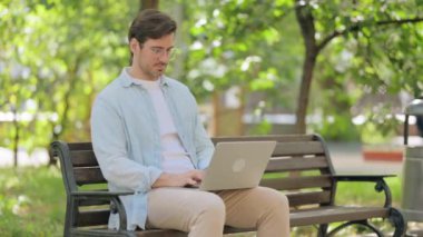 Dışarıda dizüstü bilgisayar kullanırken hasta genç adam öksürüyor.