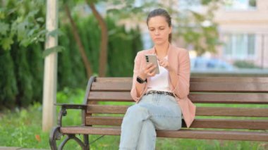 Açık havada otururken akıllı telefon kullanan sıradan bir iş kadını