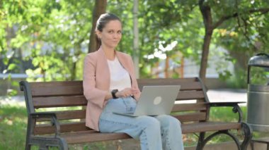 Dışarıdaki Laptop 'u kullanırken kamerayı gösteren genç kadın.