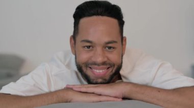 Yaşlı adam yatakta karnı üzerinde yatarken kameraya gülümsüyor.