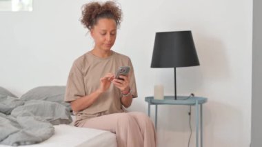 Yaşlı adam yatağın kenarında otururken akıllı telefon kullanıyor.