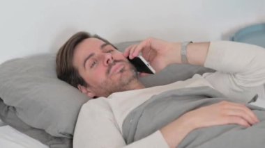 Yaşlı adam yatakta otururken telefonda konuşuyor.