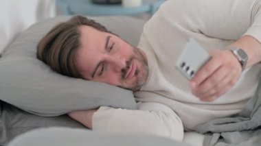Yaşlı adam yatakta yan yatarken akıllı telefon kullanıyor.