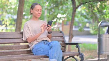 Yaşlı adam dışarıda otururken telefonda başarıyı kutluyor.