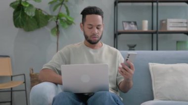 İspanyol adam dizüstü bilgisayarlı telefonu kucağında kullanıyor.