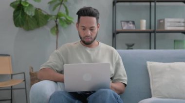 Ciddi İspanyol Adam kucağında dizüstü bilgisayarla kameraya bakıyor.