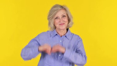 Sarı Arkaplanda Elleri Olan Yaşlı Kadın Kalp İşareti Yapıyor
