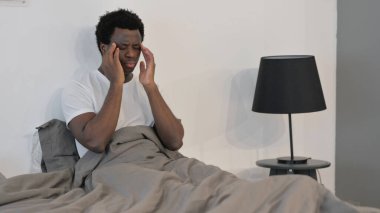 Afrikalı Adam yatakta otururken migren ağrısı çekiyor