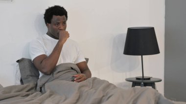 Hasta Afrikalı adam yatakta otururken öksürüyor.