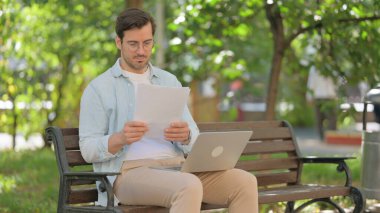 Belgeler ve laptopla çalışan sıradan bir genç adam.