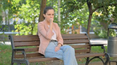 Park 'ta otururken öksüren genç kadın.