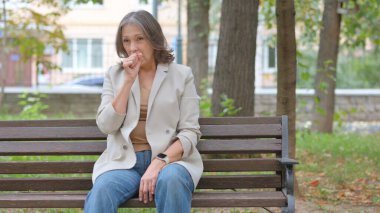 Park 'ta otururken yaşlı yaşlı yaşlı bir kadın öksürüyor.