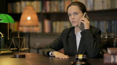 Genç bayan avukat mahkemede telefonla konuşuyor.