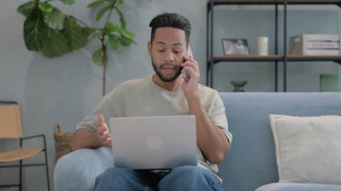 Kızgın İspanyol adam telefonda dizüstü bilgisayarla konuşuyor.