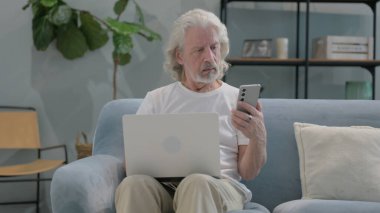 Yaşlı adam dizüstü bilgisayarlı telefonu kullanıyor.