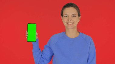 Kırmızı Arkaplanda Yeşil Ekranlı Sıradan Genç Kadın Akıllı Telefonu Gösteriyor
