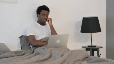 Yatakta otururken dizüstü bilgisayarda çalışırken yorgun Afrikalı Adam Uyuyor
