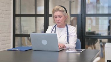 Hastanede dizüstü bilgisayarda yazı yazan kıdemli kadın doktor.