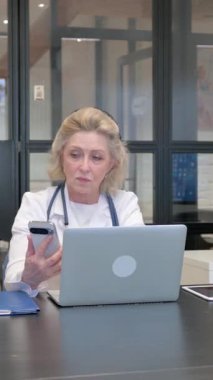 Klinikte Akıllı Telefon ve Laptop kullanan yaşlı kadın doktor.