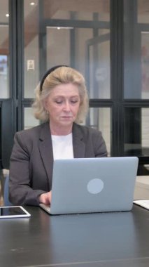 Ofiste dizüstü bilgisayarda çalışan kıdemli iş kadını.