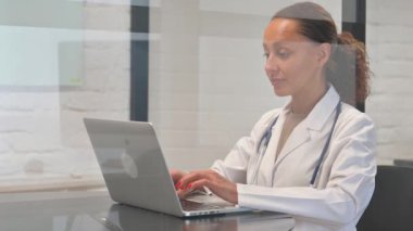 Bilgisayarda çalışırken kameraya bakan çok ırklı kadın doktor.