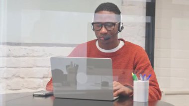 Kulaklıklı Afrikalı Laptop 'ta çalışırken kameraya bakıyor